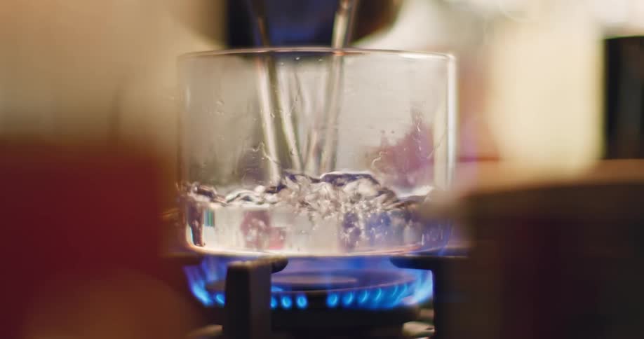 Water is poured into a clear glass pot as a gas flame of a stove ignites