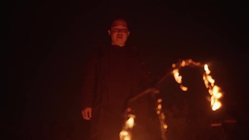 A man is standing by a burning branch at night