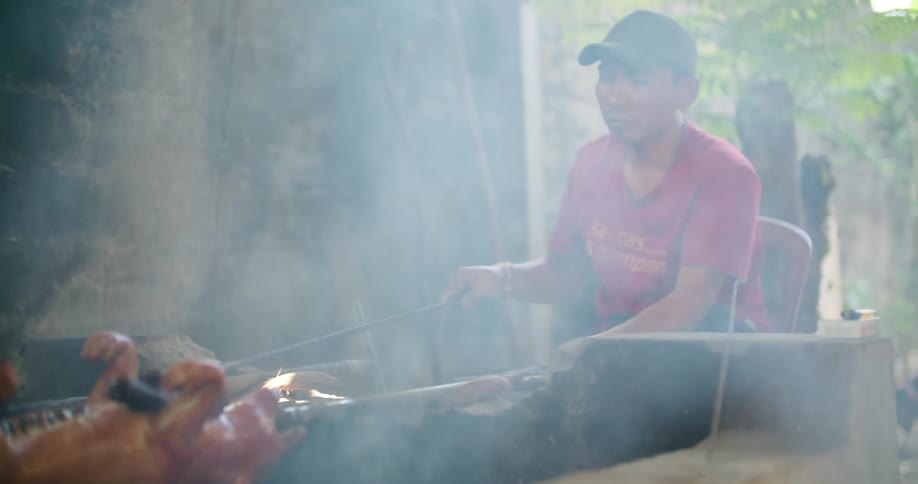 Man bastes spit pig with rag as he turns it over fire