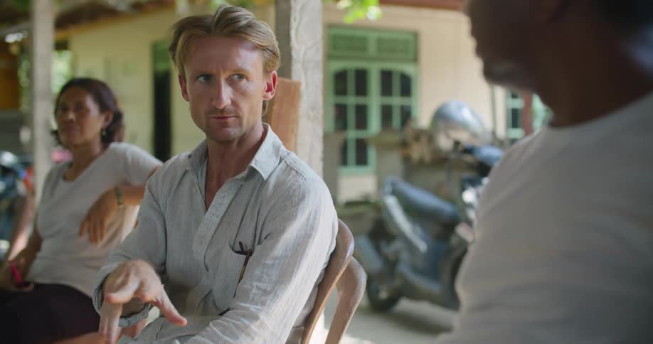 Two men sitting on plastic chairs on the porch of a tropical house talking