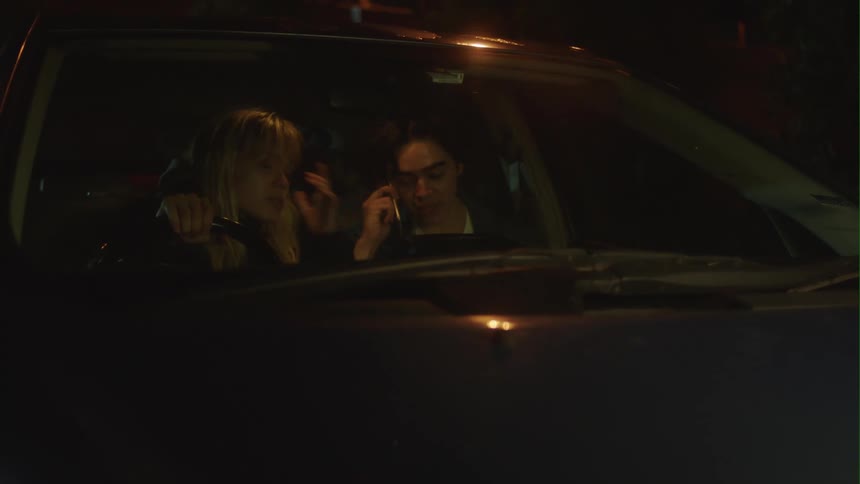 Man sitting next to a friend inside a car making a call on his smartphone at night
