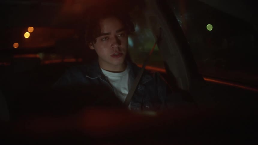 A bothered looking man talking to himself and riding in a car at night