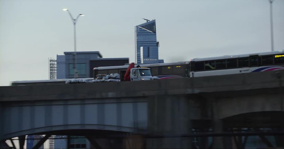 Large vehicles move along highway with city skyscrapers as a backdrop