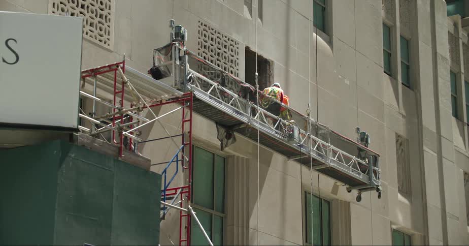 Worker standing on a suspended scaffolding on the facade of a building