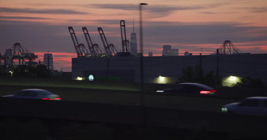 Distant view of skyscraper and high rise buildings seen from vehicle driving on highway at dusk