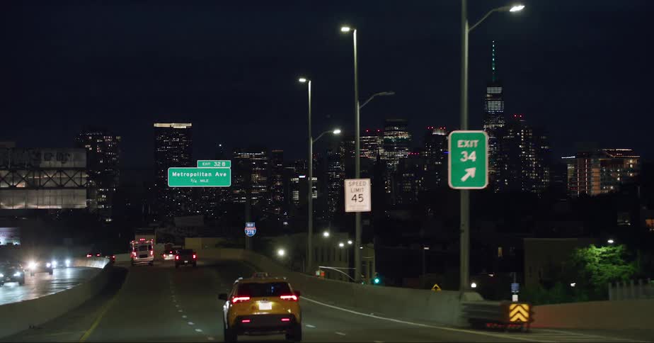 Tail lights and headlights glow in the darkness as traffic moves in and out of downtown with the city skyline shining brightly in the night sky