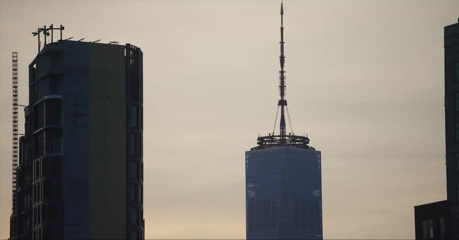 A cylindrical building with a tall antenna stands out from the rest of the tall city buildings