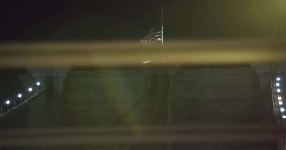 An american flag waves in the wind atop the tower of a suspension bridge