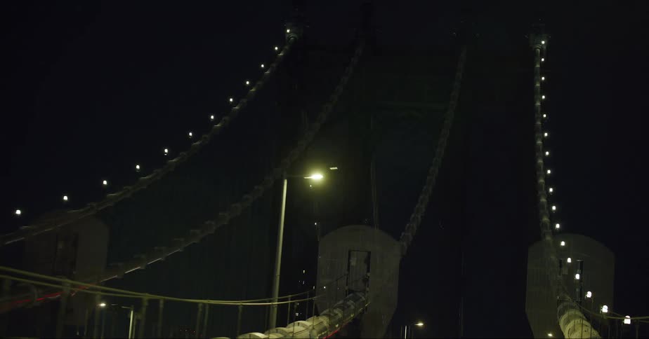 Cars traveling on a city cable bridge with lights glowing on the cables at night