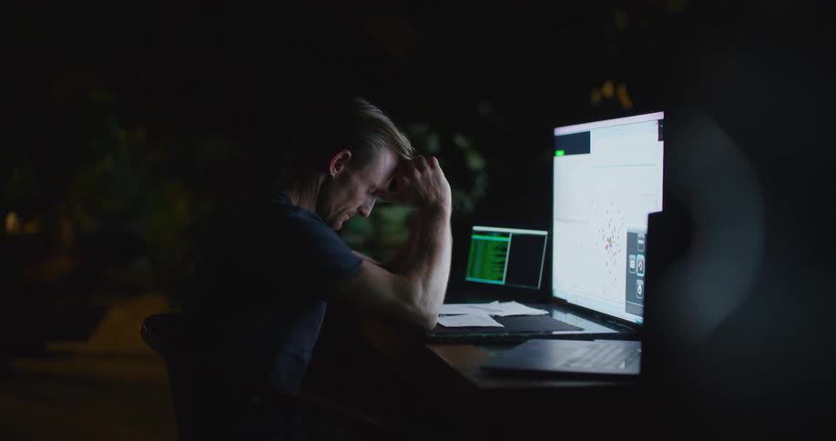 A man throws his hands up in frustration while working at his desk