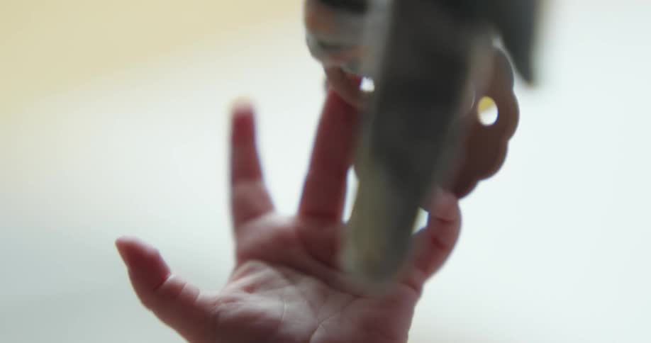 An infants hand reaching for a pacifier hanging from a ribbon