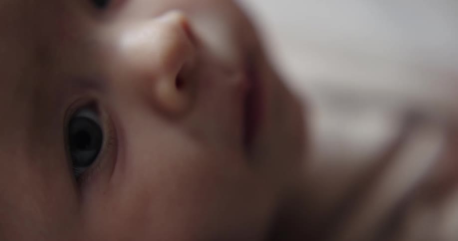 A baby lying down continues to stare even as mom rocks him with her hand