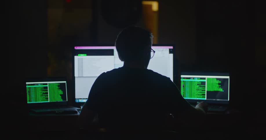 Man works while silhouetted against computers in dark room