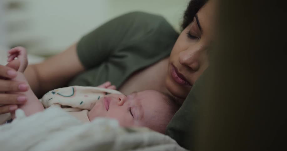 A woman is lying down sleeping with her baby and the baby wakes up