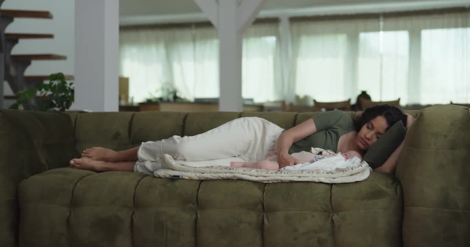 A woman sleeps next to her baby on a couch