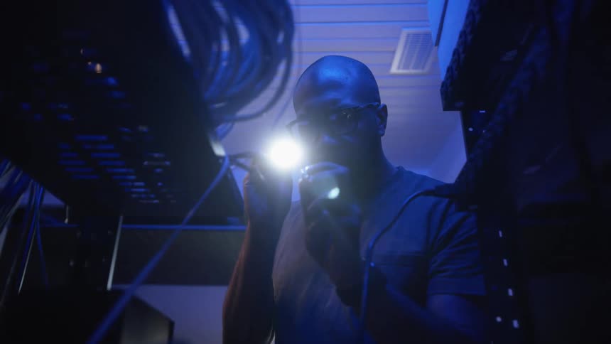 Technician shines a light over a small piece of equipment on a server rack