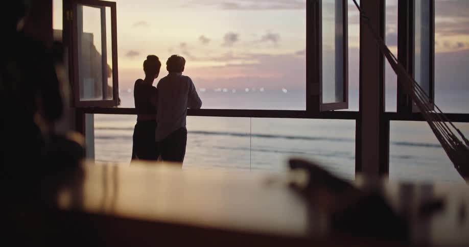 A couple stand along a railing and look at the ocean