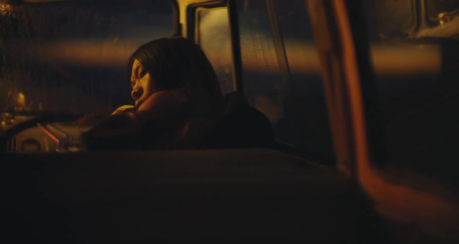 A woman trying to sleep in a car with light glowing on her face