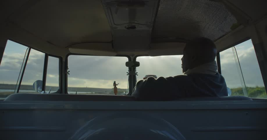 Man with grey jacket sits in classic van drinking coffee from cup