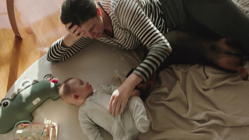 Mother with striped shirt and jeans plays with brown dog and baby lying on rug