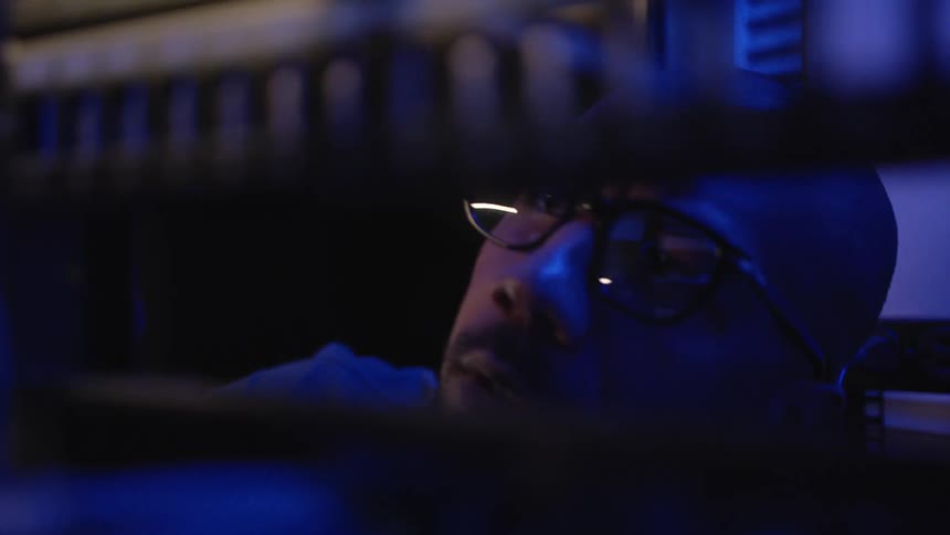 Man uses a drill to secure equipment on a rack inside a room under blue lights