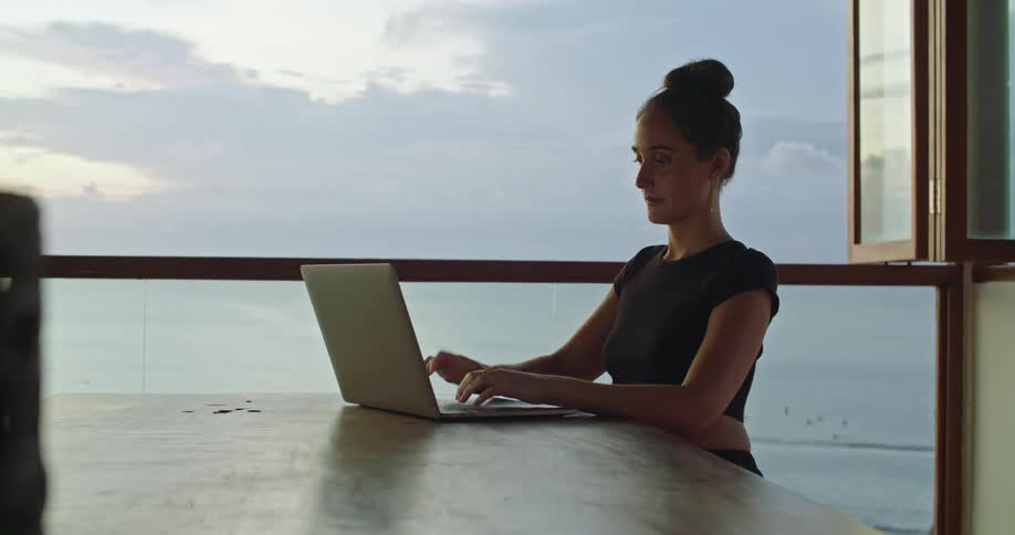 A woman types on her laptop by the open window