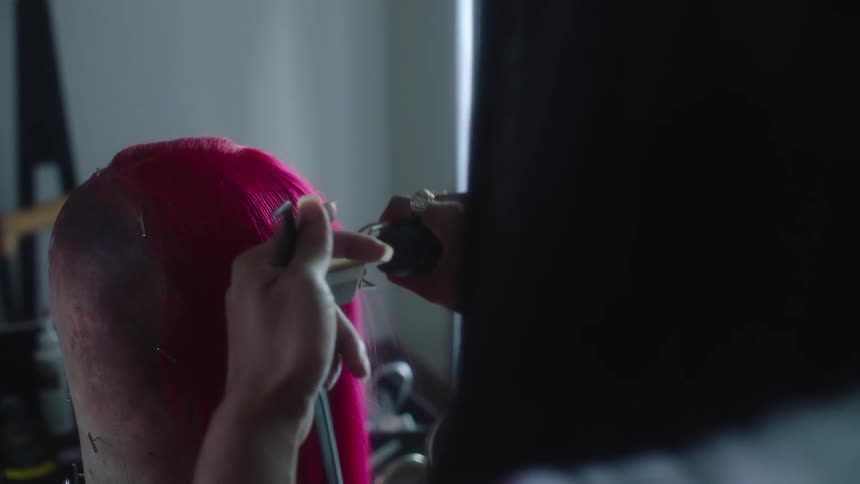 Woman combs the pink hair of a wig on a mannequin inside a room