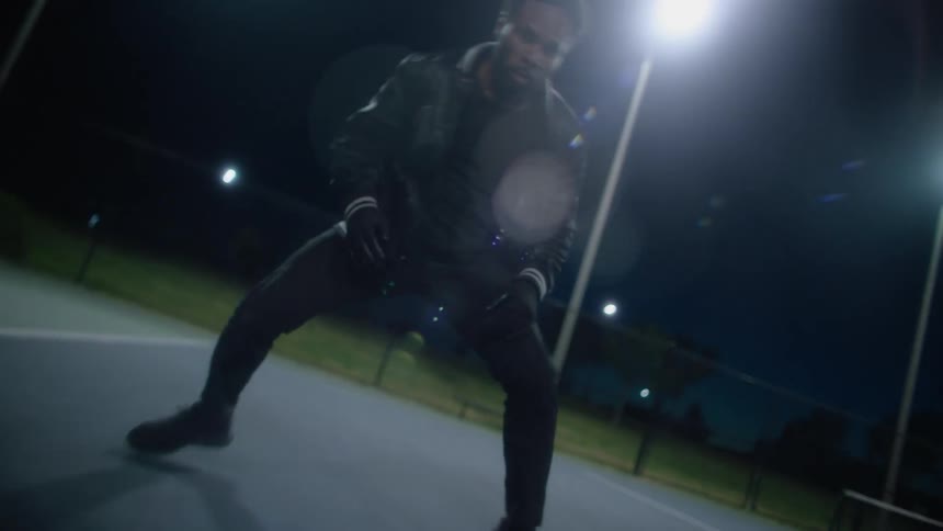 A man smiles as he dances on a basketball court at night