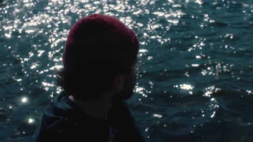A man wearing glasses and a knit cap is looking at the sparkling water as it ripples and moves