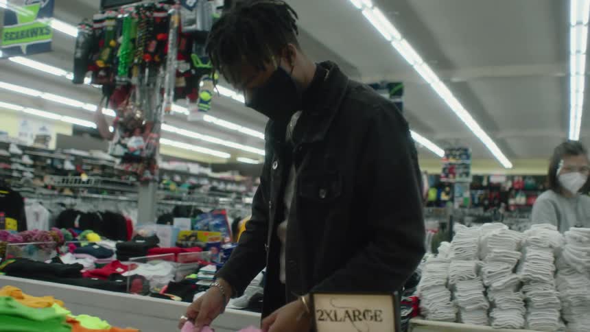 A man shops looking at items in bins while an employee restocks behind him