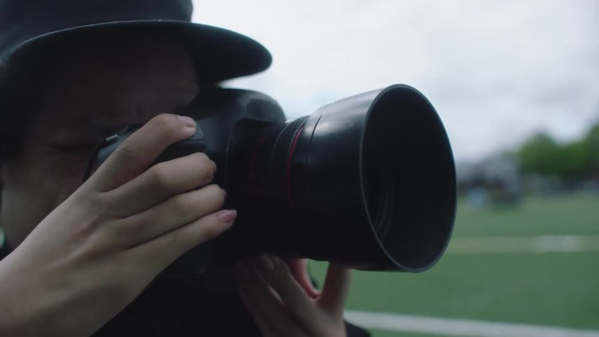 Photographer with cap and wavy hair takes photograph with camera on cloudy day