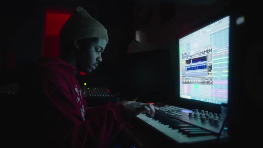 A teenager plays on a keyboard while viewing a computer monitor displaying an editing program