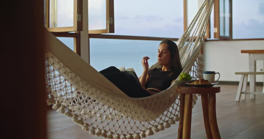 Woman eating seafood relaxing on a hammock on a beachfront apartment