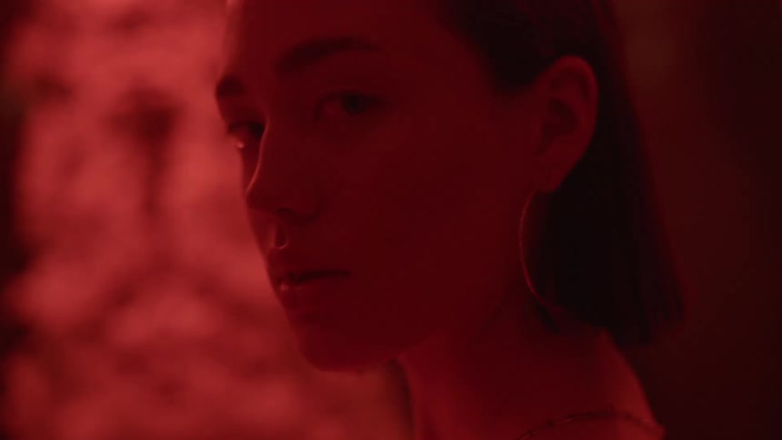 A young woman under red lighting turns her head to look into the camera