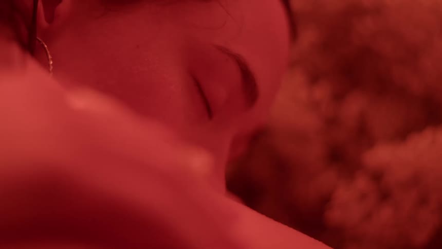 In a place illuminated with red light a woman is lying face down and she closes her eyes