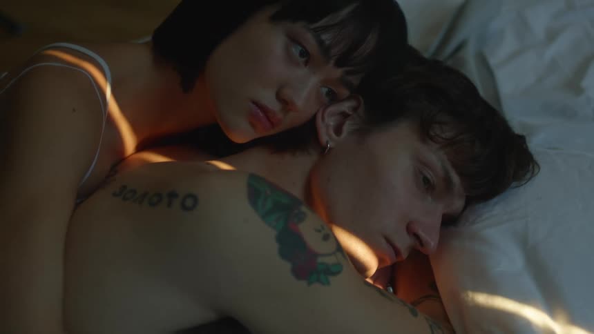 A sad looking man and woman lie in be cuddled together