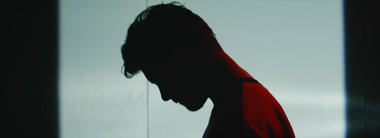 A man stands with his head bowed in front of a screen