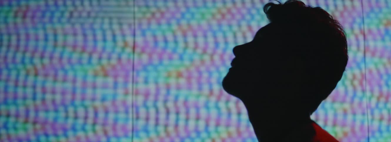 Man with white shirt lifting his head up is silhouetted against the large screen