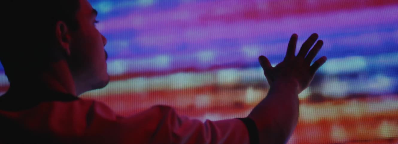 A man holds his hand up to a large display screen that is showing mostly static and distortion