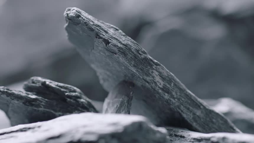Smoke rises near stone slab leaning on narrow rock with large boulders in the background