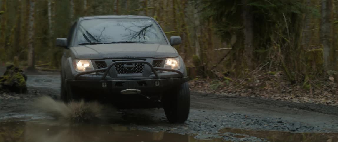 A man driving a truck through a forest drives through a large puddle and splashes mud
