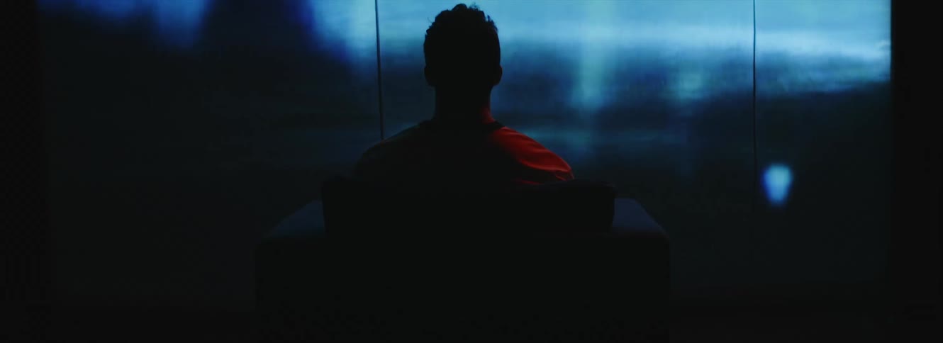 A man sitting in a chair looks up at a large screen with fuzzy images