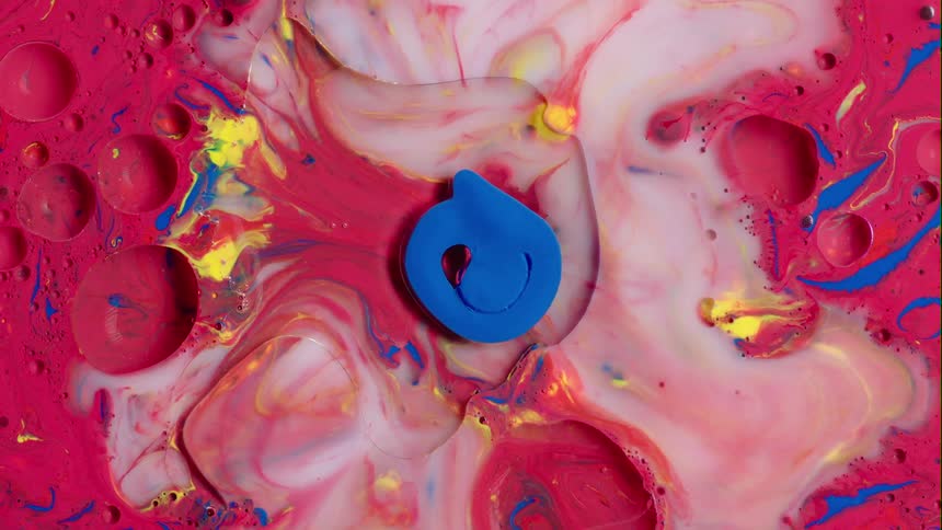A blue blob sits inside of a red liquid substance with blue and yellow drops and as it echos and moves a white substance emerges from the middle