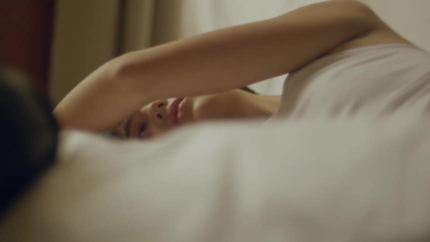 Woman lies on her side on the bed with another person