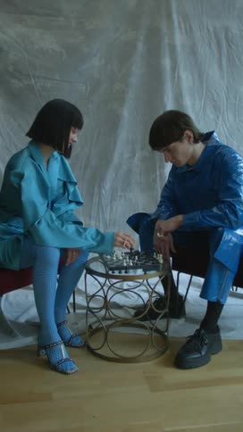 A man and woman play chess on a small iron table