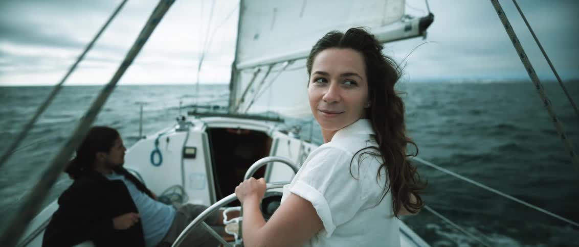 A woman sails a boat and looks back at the shore behind her