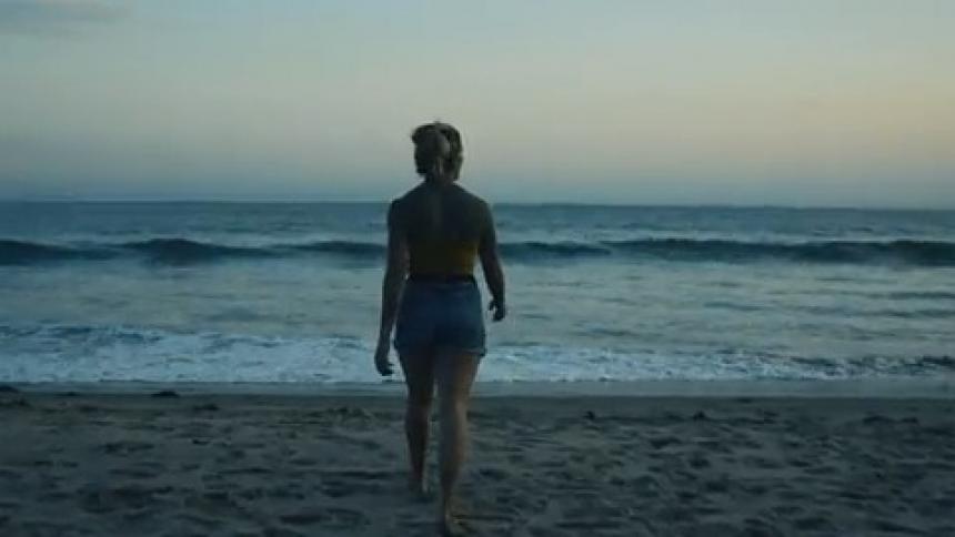 Female acrobat walks across beach toward water and performs two flips