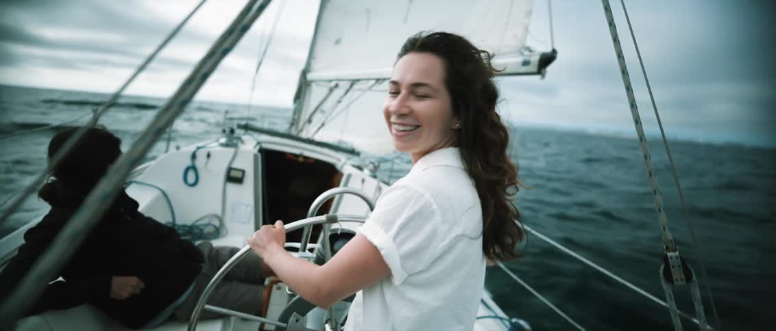 Woman sailing in the ocean looks back at land and smiles