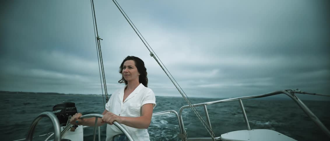 A woman steers a sailboat through the ocean on a cloudy day