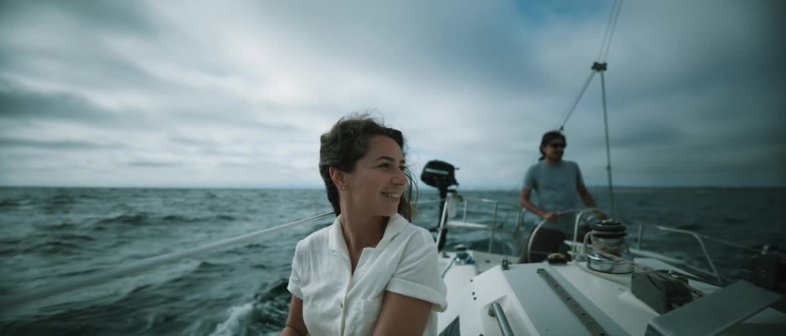 A woman on a sailboat looks out at dolphins in the distance